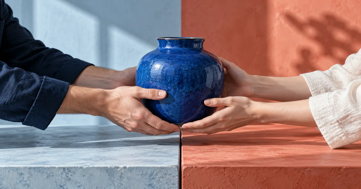 A cobalt ceramic vessel passes between hands over blue and coral worktables